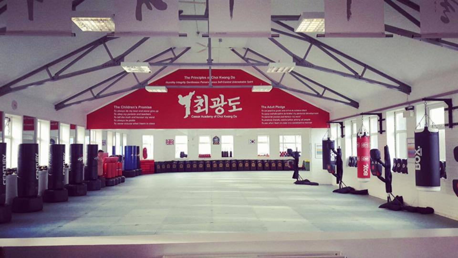 A spacious martial arts training hall with high ceilings, exposed beams, and abundant natural light from large windows.