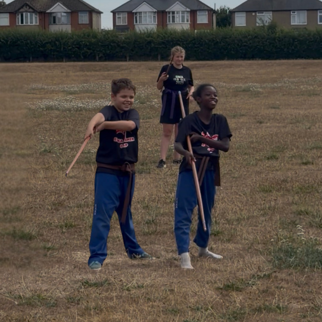 Students training with wooden bo staffs outdoors