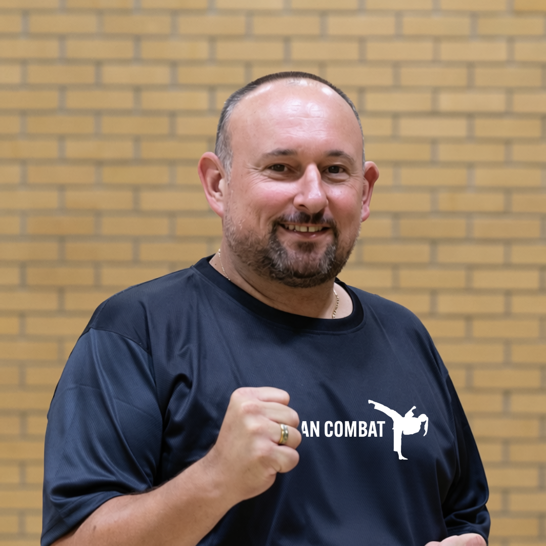 Portrait of an adult man smiling at the camera against a plain yellow-brick wall.