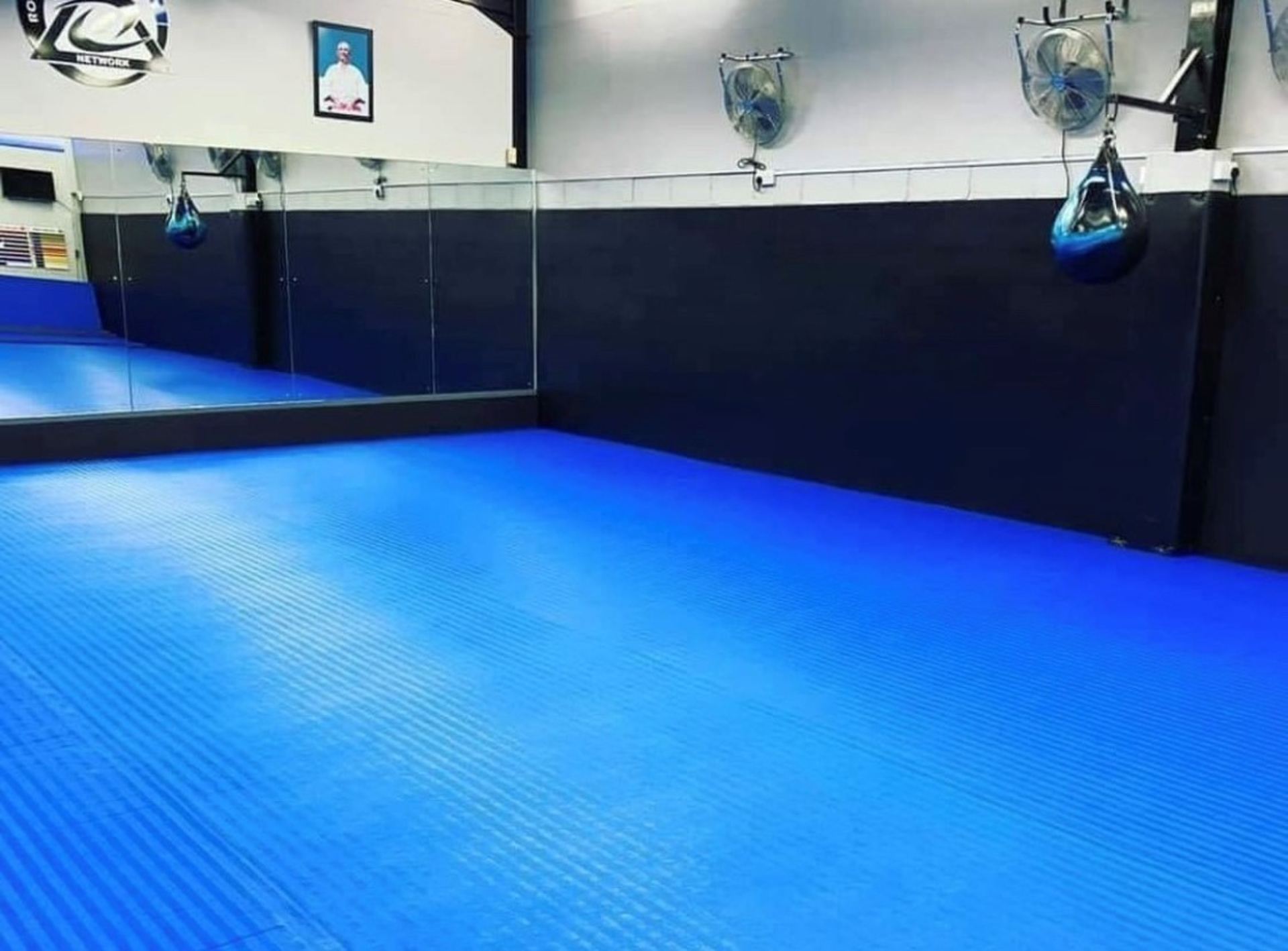 The training mats at PMA Caernarfon — blue matted dojo with mirrors, punch bags and fans